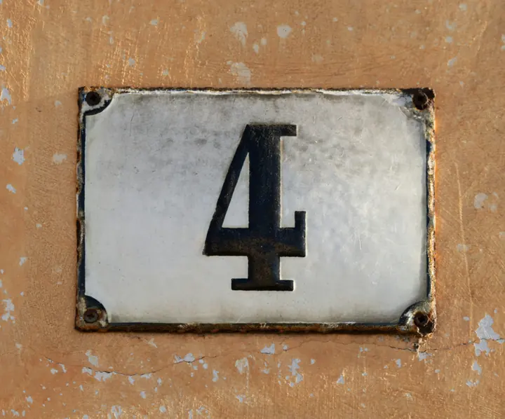 A weathered enamel house number plate with a black 4, screwed to a rendered wall.