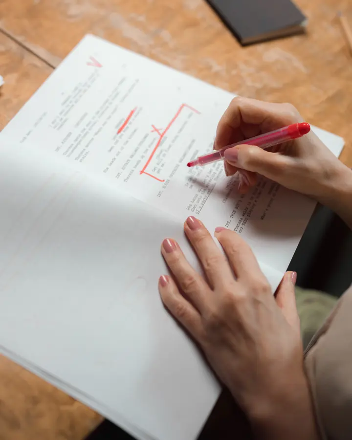 A hand marking up a typed page in red pen: a line struck out, a passage bracketed.