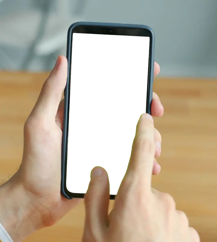 Two hands holding a phone over a wooden table, a thumb on the screen.