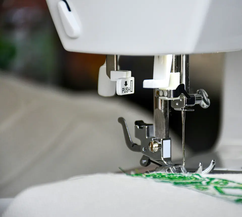 A sewing machine needle stitching a green pattern into white fabric.