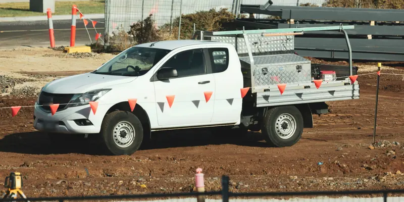 A white tray-back ute with a toolbox, parked on a building site behind safety bunting.